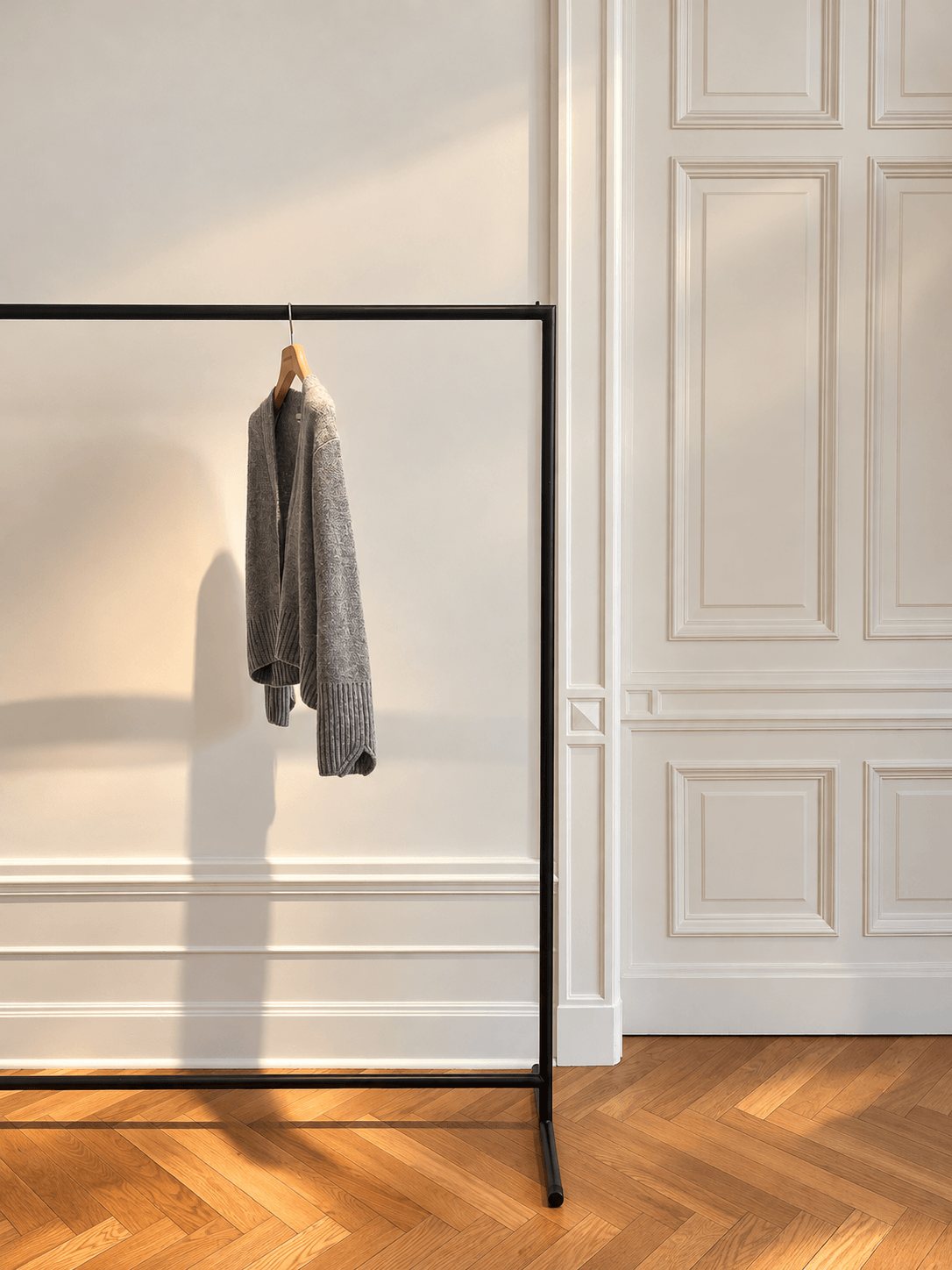 A grey cashmere cardigan on a black rail in front of panelled walls